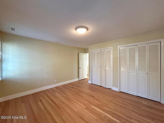 unfurnished bedroom with visible vents, baseboards, light wood-type flooring, and multiple closets