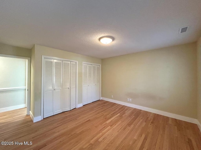 unfurnished bedroom featuring baseboards, light wood-style floors, visible vents, and multiple closets