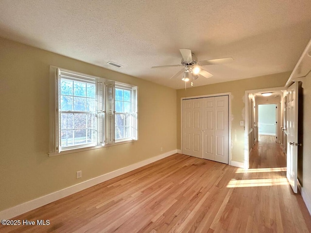 unfurnished bedroom featuring visible vents, a textured ceiling, a closet, light wood-style floors, and baseboards