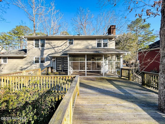 back of property with a wooden deck, a sunroom, and a chimney