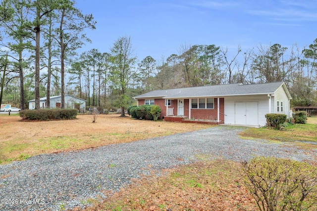 ranch-style house featuring brick siding, a porch, gravel driveway, and a garage