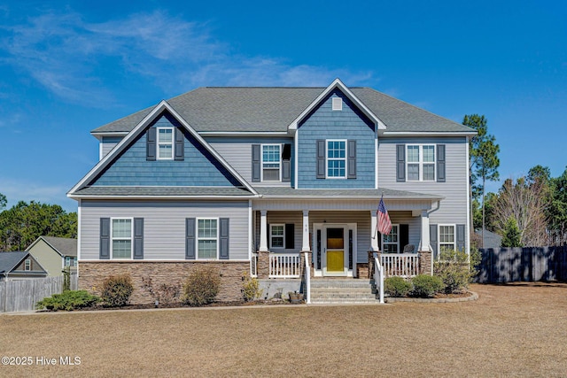 craftsman house with stone siding, covered porch, a shingled roof, and fence