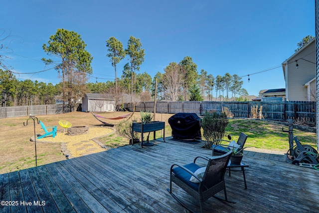 wooden terrace with a lawn, a fenced backyard, a fire pit, a grill, and an outdoor structure