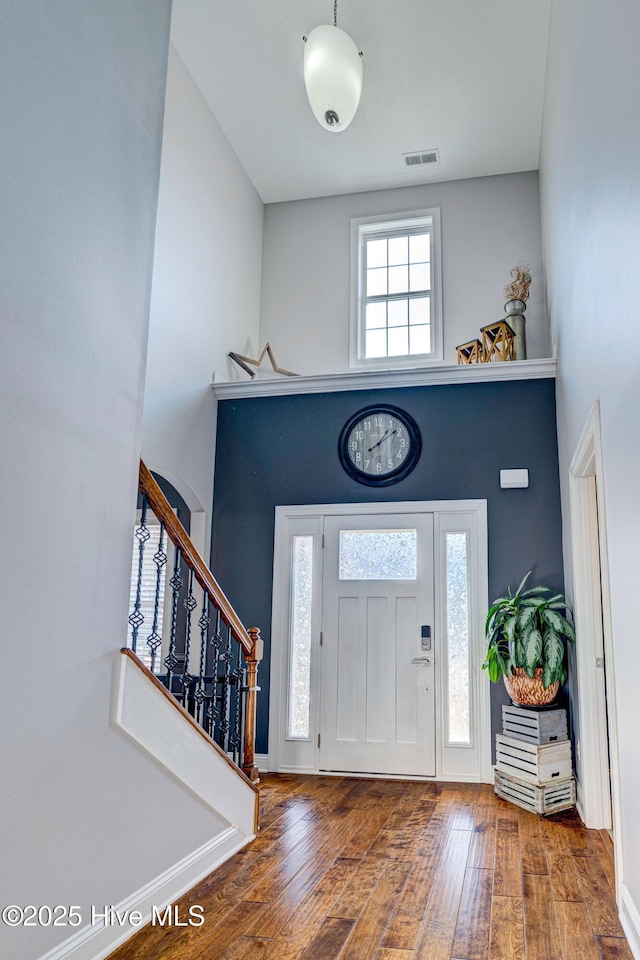 entrance foyer with hardwood / wood-style floors, stairway, a high ceiling, and visible vents