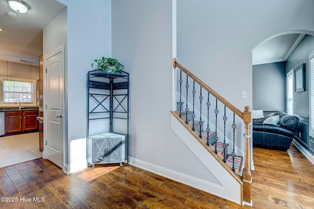 stairway with hardwood / wood-style floors, baseboards, arched walkways, and ornamental molding