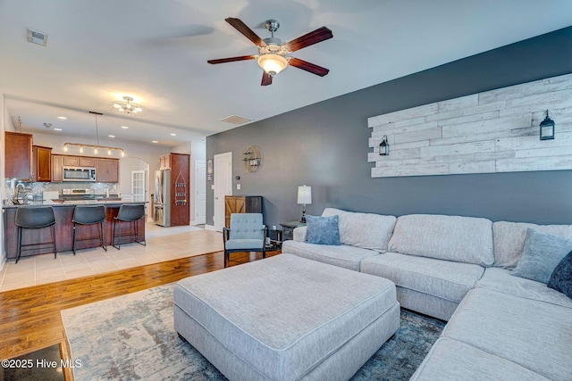 living room with ceiling fan, visible vents, arched walkways, and light wood-style flooring