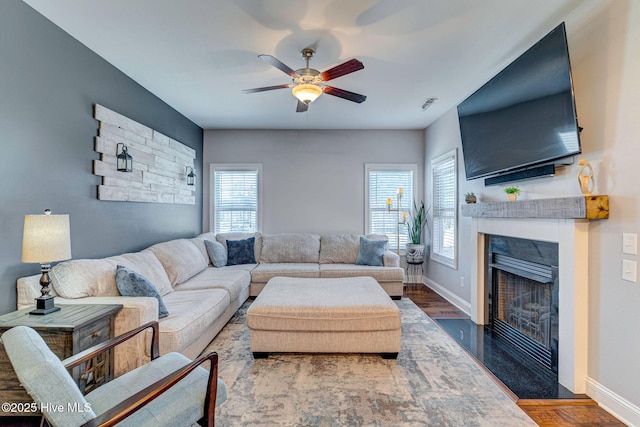 living area featuring baseboards, a fireplace with flush hearth, wood finished floors, and a ceiling fan