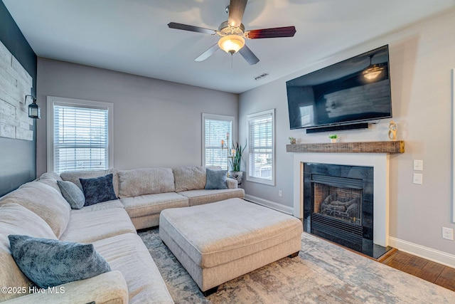 living area featuring visible vents, a fireplace with raised hearth, wood finished floors, baseboards, and ceiling fan