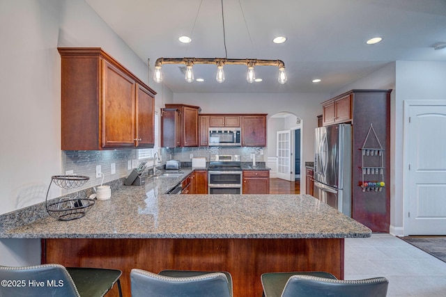 kitchen with arched walkways, backsplash, a peninsula, and stainless steel appliances