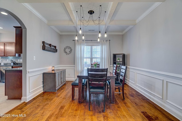 dining space featuring beamed ceiling, a wainscoted wall, light wood-style floors, arched walkways, and coffered ceiling