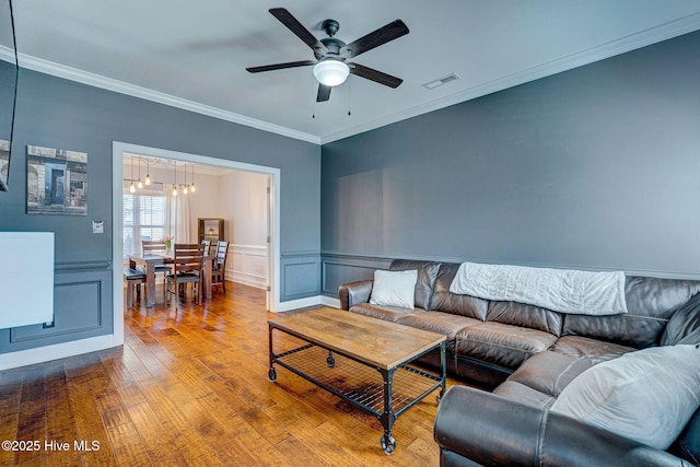 living area with hardwood / wood-style floors, visible vents, wainscoting, crown molding, and ceiling fan with notable chandelier