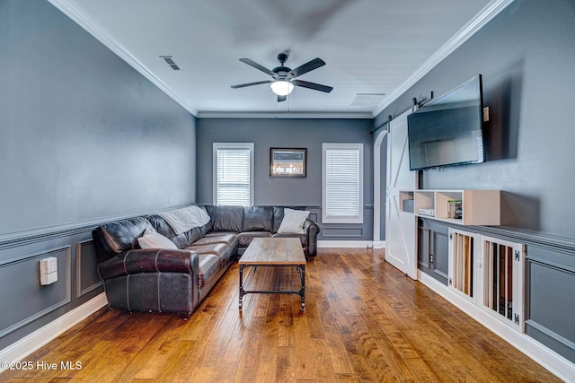 living room featuring visible vents, crown molding, ceiling fan, a barn door, and hardwood / wood-style floors