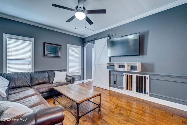 living area with a wainscoted wall, ornamental molding, wood finished floors, a barn door, and ceiling fan