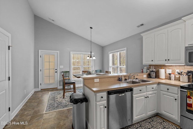 kitchen featuring visible vents, a peninsula, a sink, stainless steel appliances, and white cabinetry