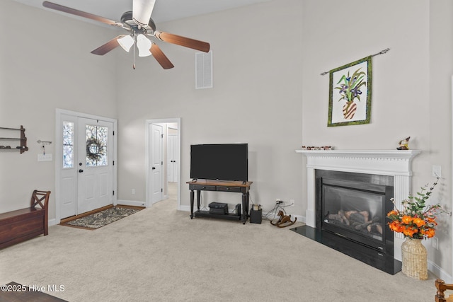 carpeted living area with visible vents, a fireplace with flush hearth, a high ceiling, and baseboards