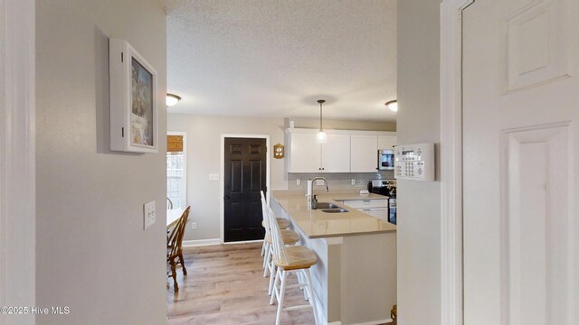 kitchen with a sink, a kitchen breakfast bar, appliances with stainless steel finishes, white cabinets, and decorative backsplash