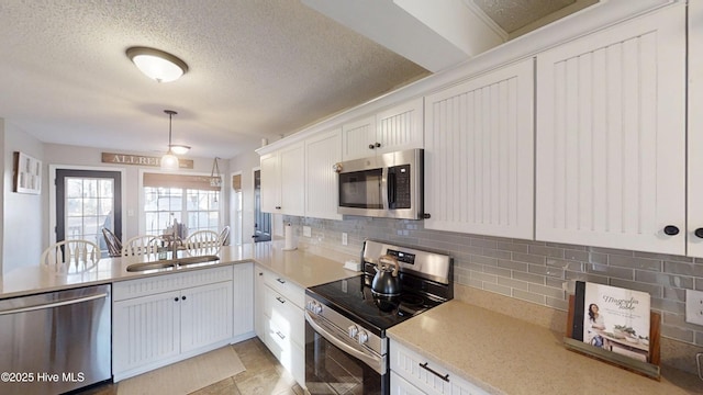 kitchen featuring a sink, backsplash, stainless steel appliances, a peninsula, and white cabinets