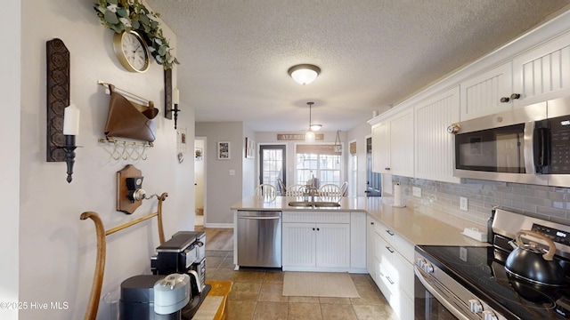 kitchen with a peninsula, a sink, stainless steel appliances, white cabinetry, and backsplash