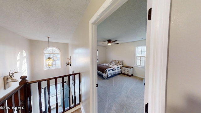 hallway featuring carpet flooring, an upstairs landing, baseboards, and a textured ceiling