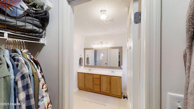 full bathroom featuring tile patterned flooring, double vanity, a textured ceiling, and a sink