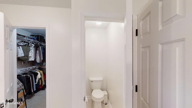 bathroom with a spacious closet, toilet, and baseboards