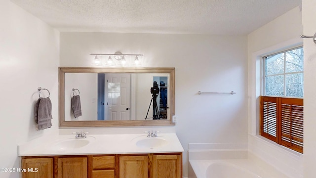 bathroom with a bath, double vanity, a textured ceiling, and a sink