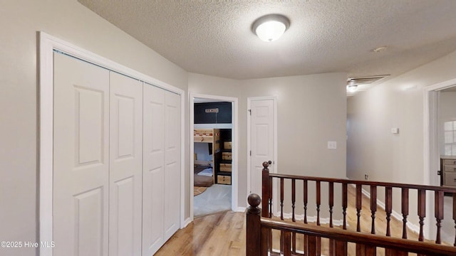 corridor featuring light wood-style flooring, an upstairs landing, and a textured ceiling