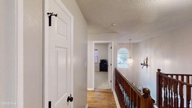 hall with an upstairs landing, light wood-style floors, baseboards, and a textured ceiling