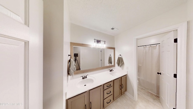 bathroom with a sink, visible vents, a textured ceiling, and double vanity