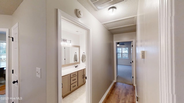 hallway with visible vents, baseboards, attic access, and light wood finished floors