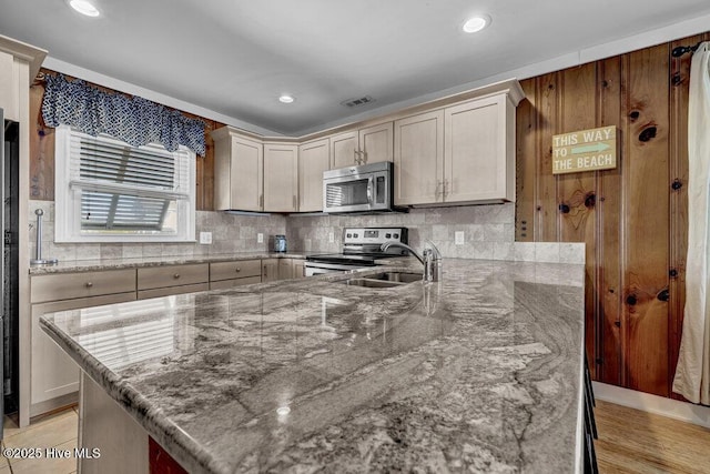 kitchen featuring light stone countertops, a peninsula, a sink, decorative backsplash, and appliances with stainless steel finishes