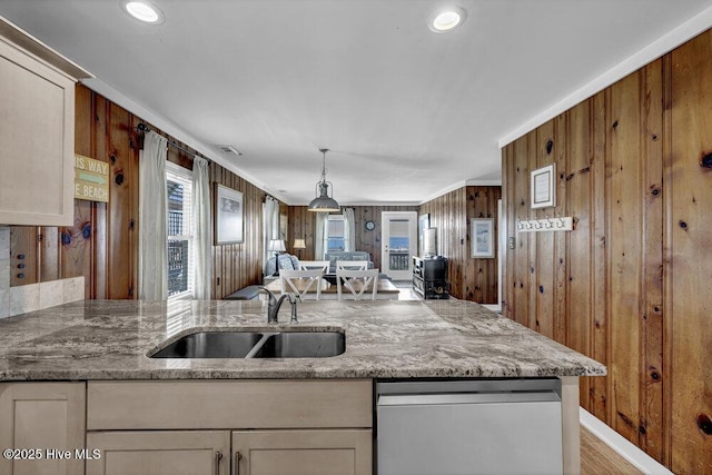 kitchen with pendant lighting, a sink, stainless steel dishwasher, wooden walls, and light stone countertops