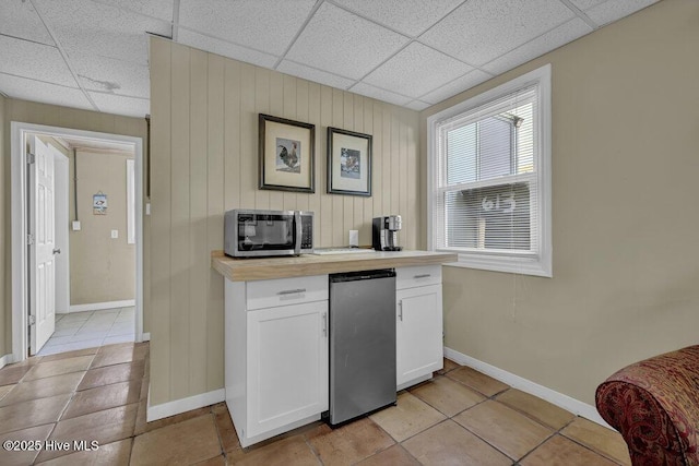 kitchen featuring refrigerator, light countertops, white cabinets, a paneled ceiling, and stainless steel microwave