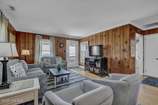 living area with light wood-type flooring, visible vents, and wood walls