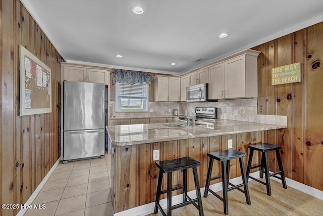 kitchen with a peninsula, backsplash, wood walls, and appliances with stainless steel finishes