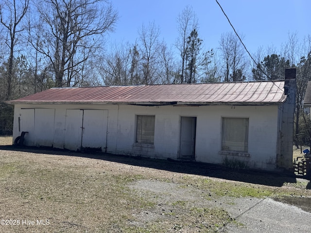 view of front of house with a chimney, concrete block siding, and metal roof