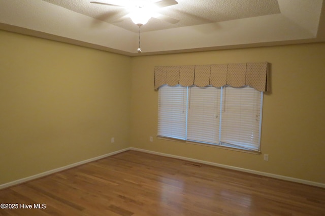 unfurnished room with baseboards, a raised ceiling, ceiling fan, and wood finished floors