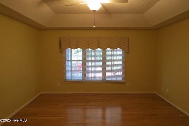 unfurnished room with a tray ceiling, a textured ceiling, wood finished floors, and a ceiling fan