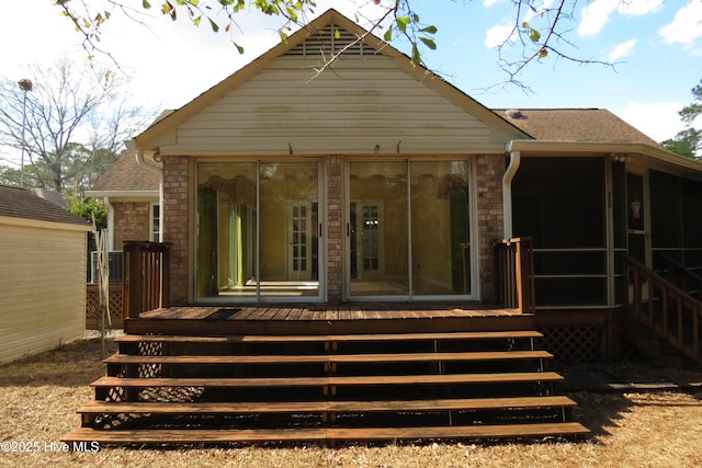 back of property with brick siding, a shingled roof, and a sunroom