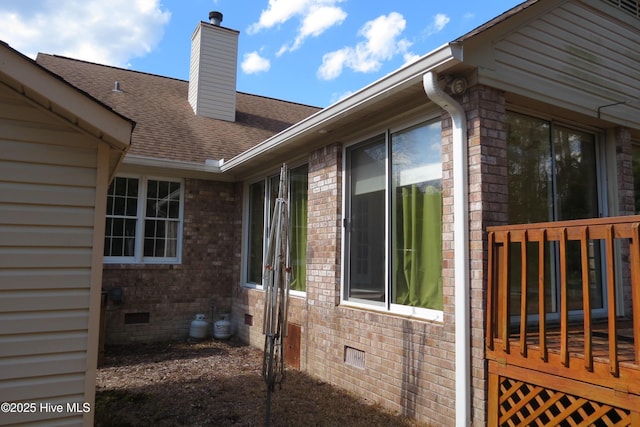 view of side of home featuring a chimney, brick siding, roof with shingles, and crawl space