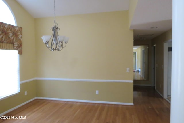 spare room with an inviting chandelier, wood finished floors, and baseboards