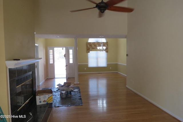 unfurnished living room with wood finished floors, baseboards, a fireplace, a towering ceiling, and ceiling fan with notable chandelier