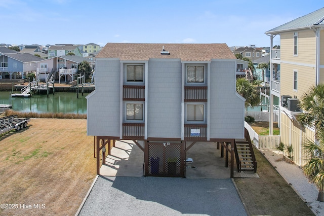 exterior space featuring roof with shingles, central AC, a water view, a lawn, and a residential view