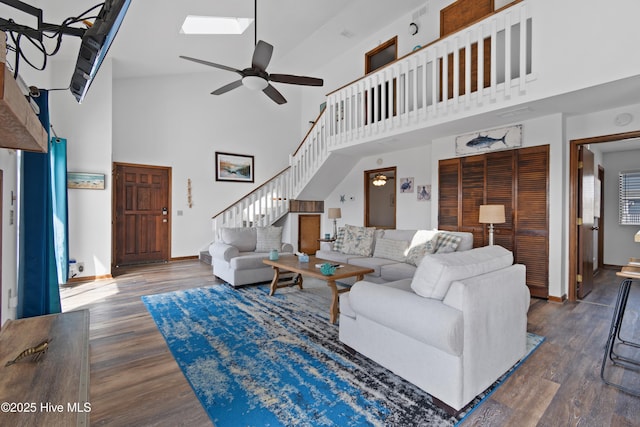 living room with a skylight, stairs, a ceiling fan, and wood finished floors