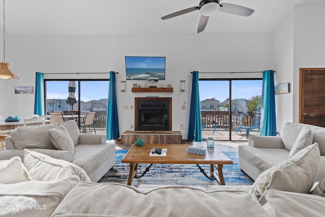 living room with wood finished floors, plenty of natural light, a fireplace with raised hearth, and ceiling fan