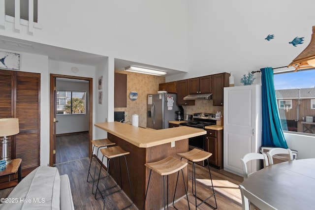 kitchen featuring under cabinet range hood, wood finished floors, appliances with stainless steel finishes, a breakfast bar area, and light countertops