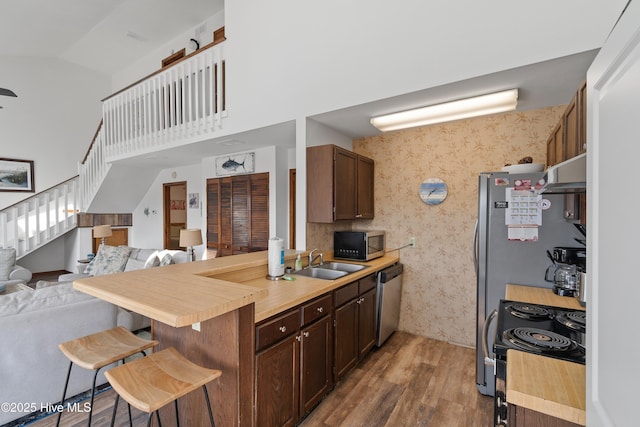 kitchen with a sink, under cabinet range hood, appliances with stainless steel finishes, a kitchen breakfast bar, and open floor plan