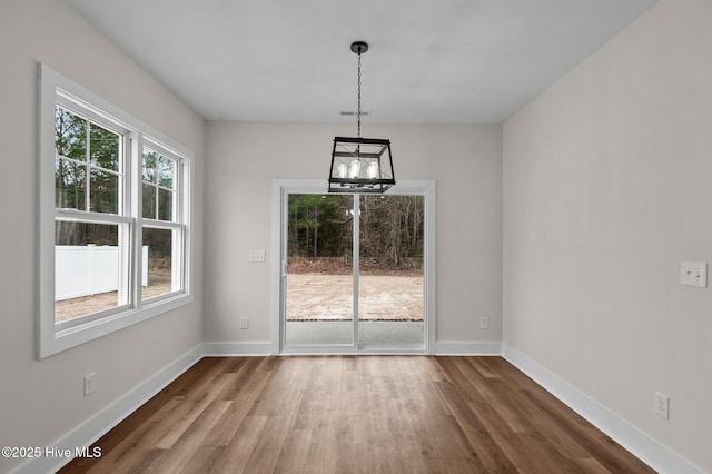 unfurnished dining area featuring an inviting chandelier, wood finished floors, and baseboards