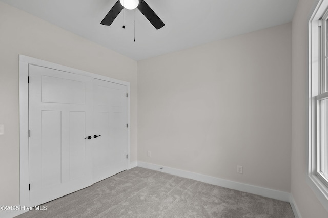 unfurnished bedroom featuring baseboards, light carpet, a closet, and a ceiling fan