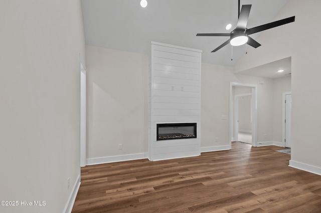 unfurnished living room featuring a ceiling fan, a large fireplace, baseboards, and wood finished floors